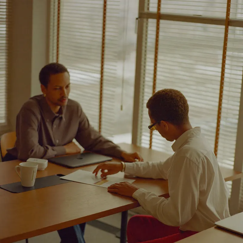 Un consultant explique un document à un client autour d'une table en bois.