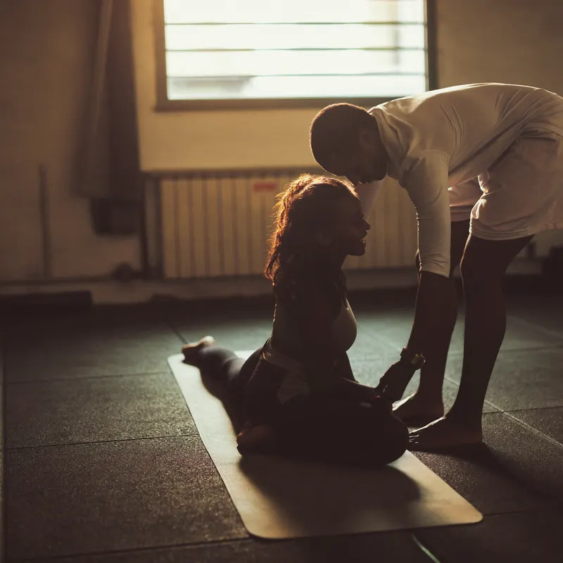 Un coach guide l'étirement d'une cliente dans une petite salle de sport.